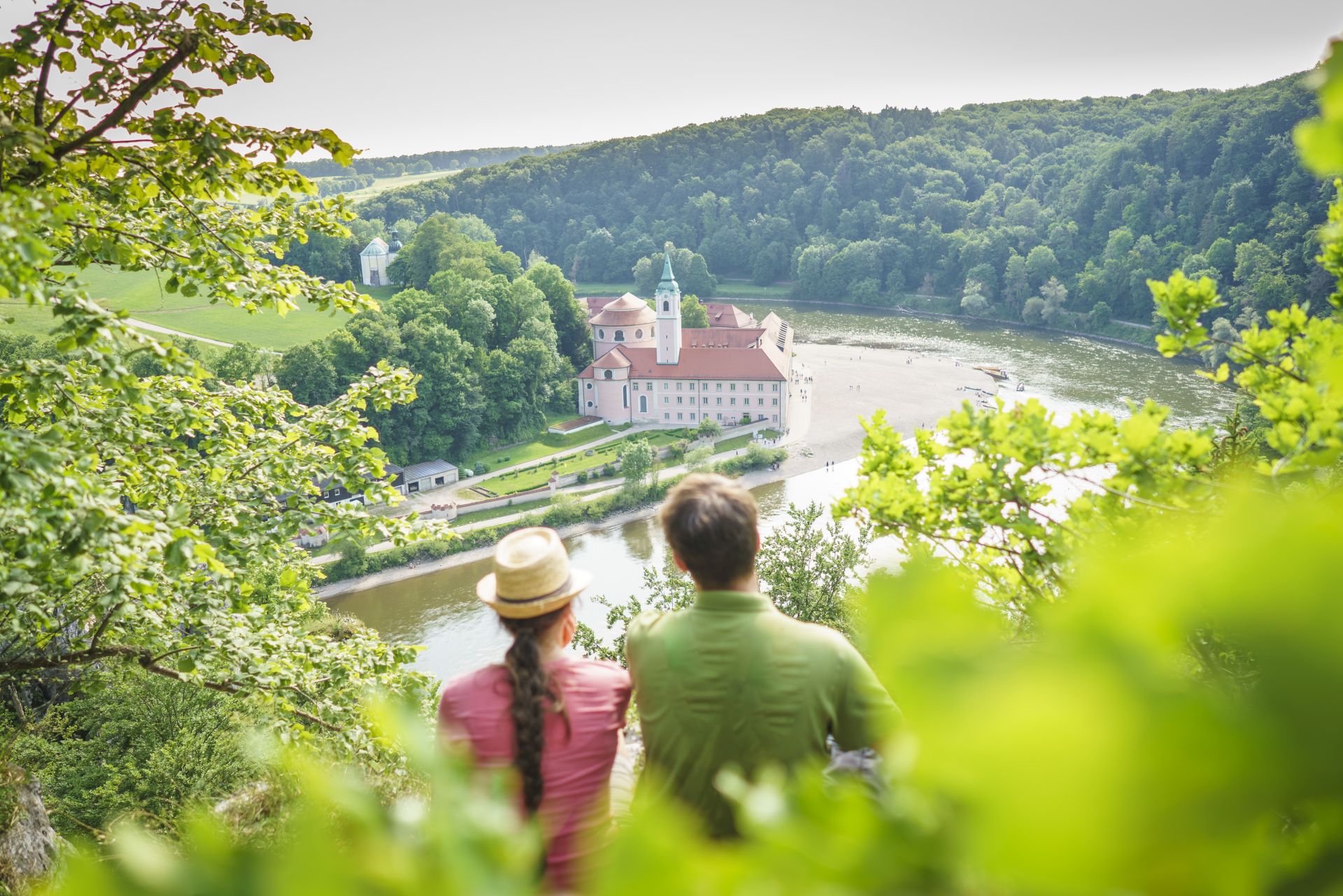 Ein Wanderpärchen blickt von oben auf die Donau und das Kloster Weltenburg.