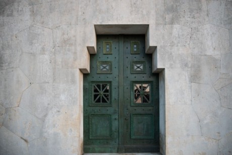 Das Bild zeigt eine grüne, metallene Tür eingelassen in schwere Steinquader.
