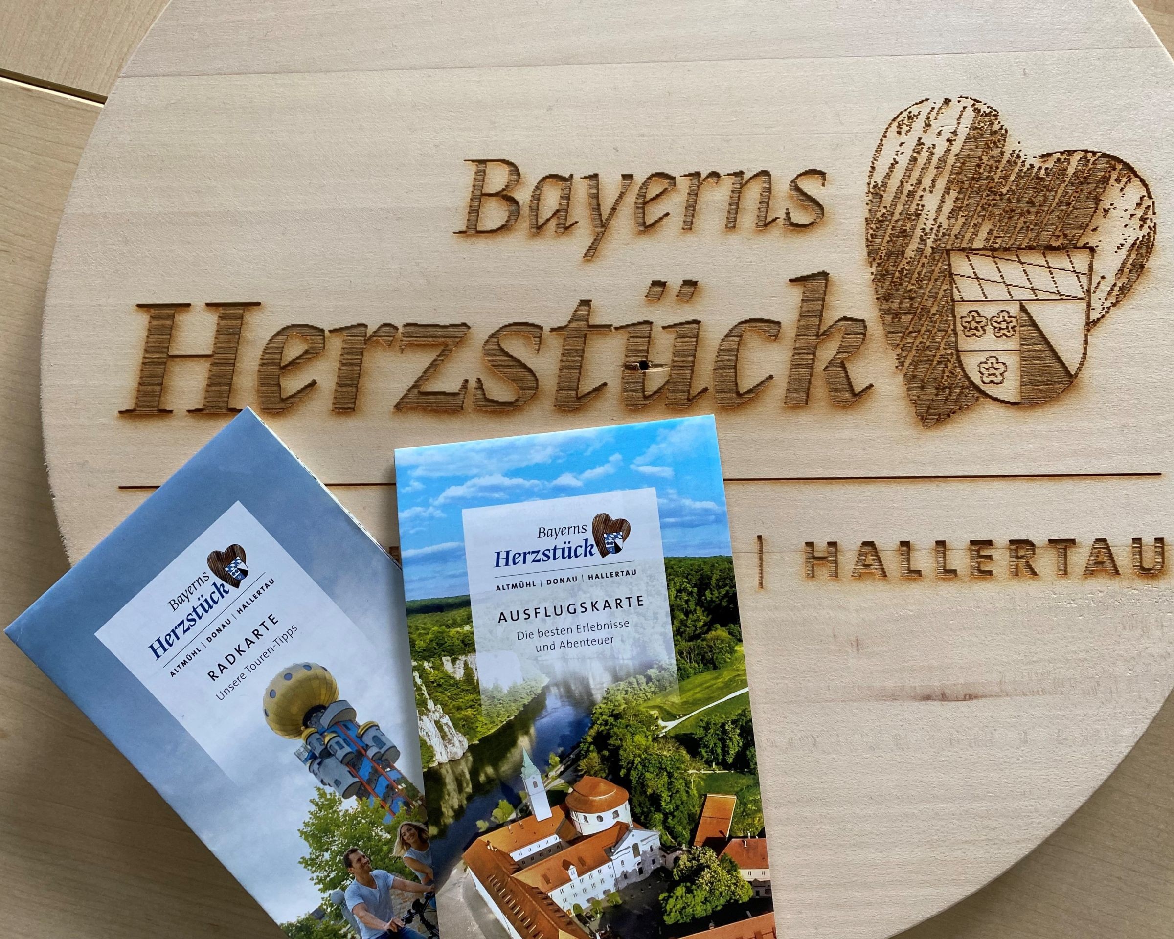 Auf einem Holzbrett mit dem Schriftzug "Bayerns Herzstück" liegen zwei Prospekte der Urlaubsregion Kelheim.