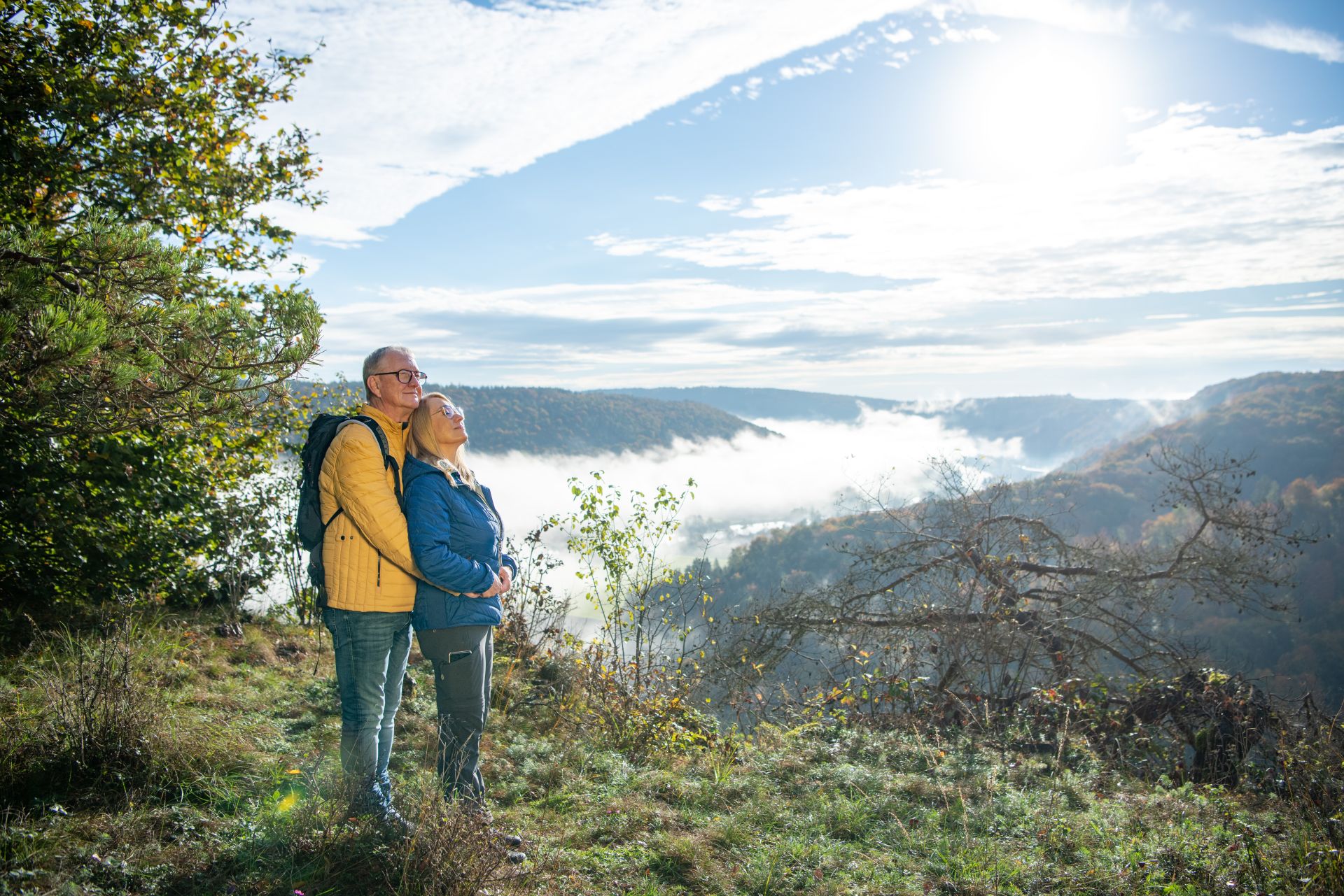 Ein Paar genießt bei einer Wanderung auf dem Roßkopfsteig Riedenburg einen Moment der Stille. Hinter ihnen steigt der Nebel zwischen den Hängen des Altmühltals auf.