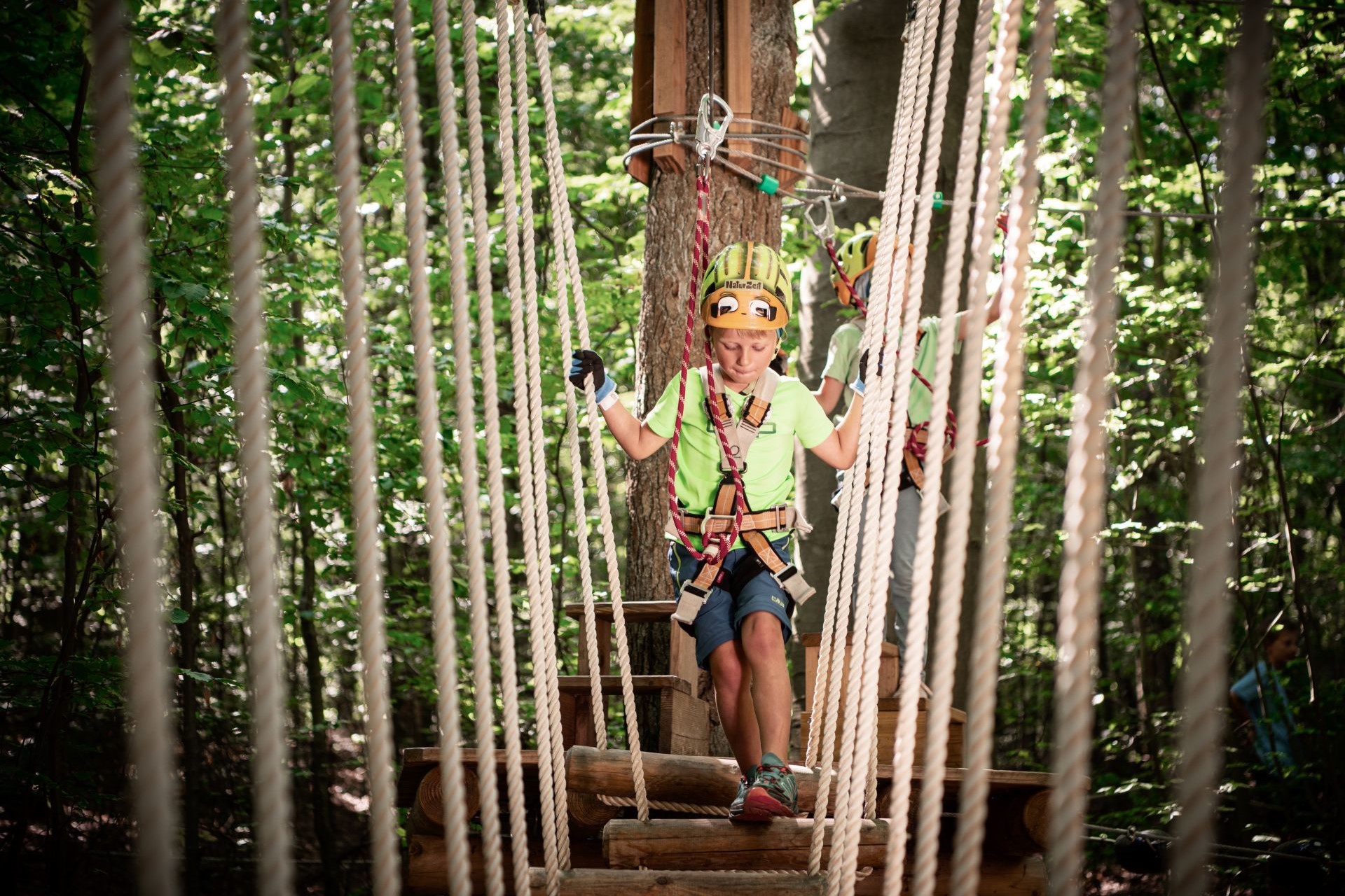 Ein Junge mit Helm und Sicherungsgurten klettert zwischen Seilen hindurch im Klettergarten.