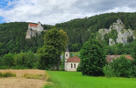 Die Burg Prunn steht auf einem mit Bäumen umgebenen Felsen. Im Tal steht eine Kapelle.