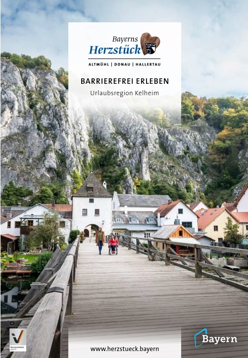 Titelseite der Broschüre "Barrierefrei erleben". Zu sehen ist eine Rollstuhlfahrerin mit Begleitung auf der Holzbrücke in Essing. Sie gehen auf den Ort mit seiner imposanten Felswand zu.
