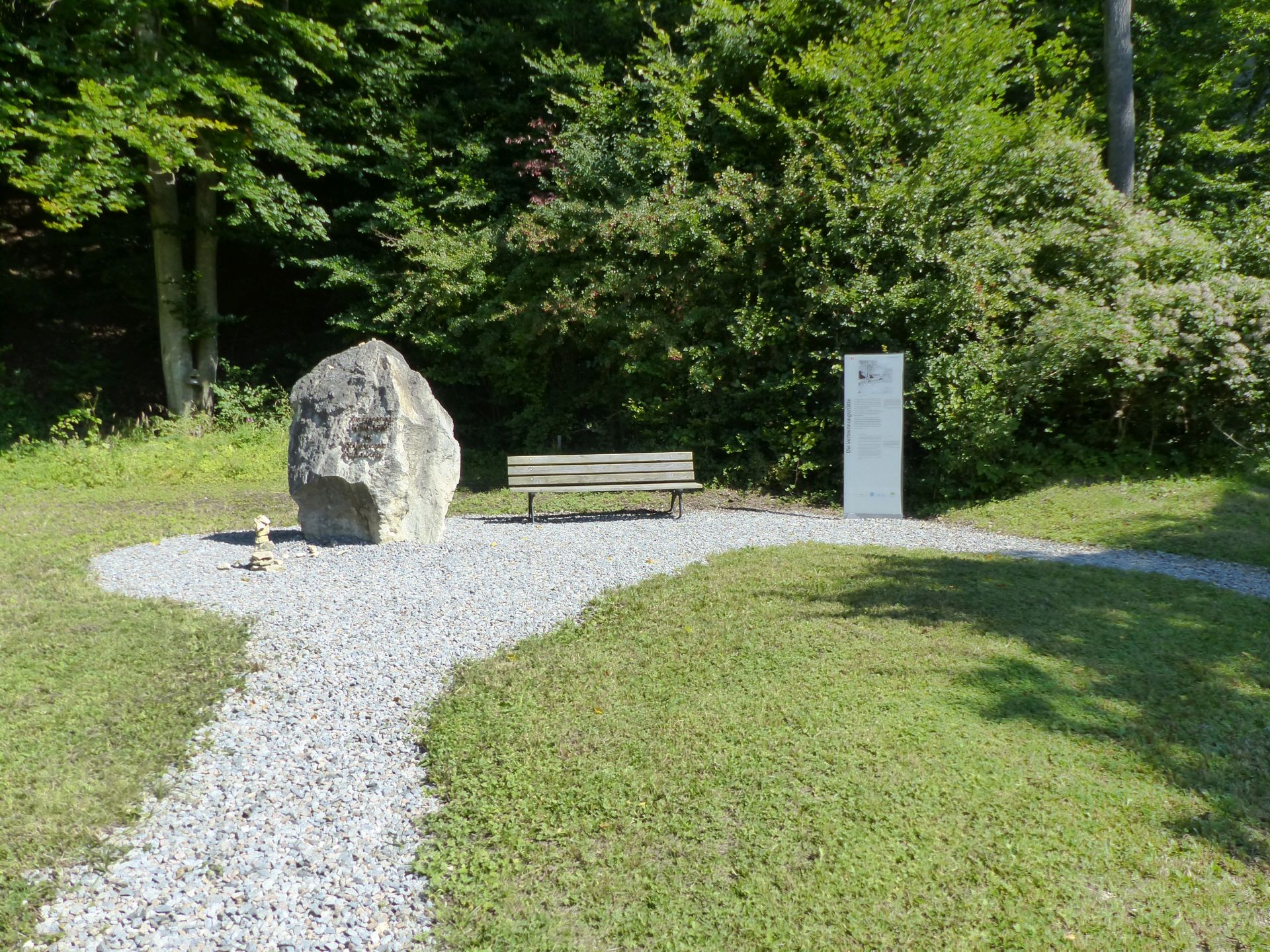 Neben einer Parkbank und einem großen, runden Stein steht eine Schautafel des Gedenkwegs Saal a.d.Donau
