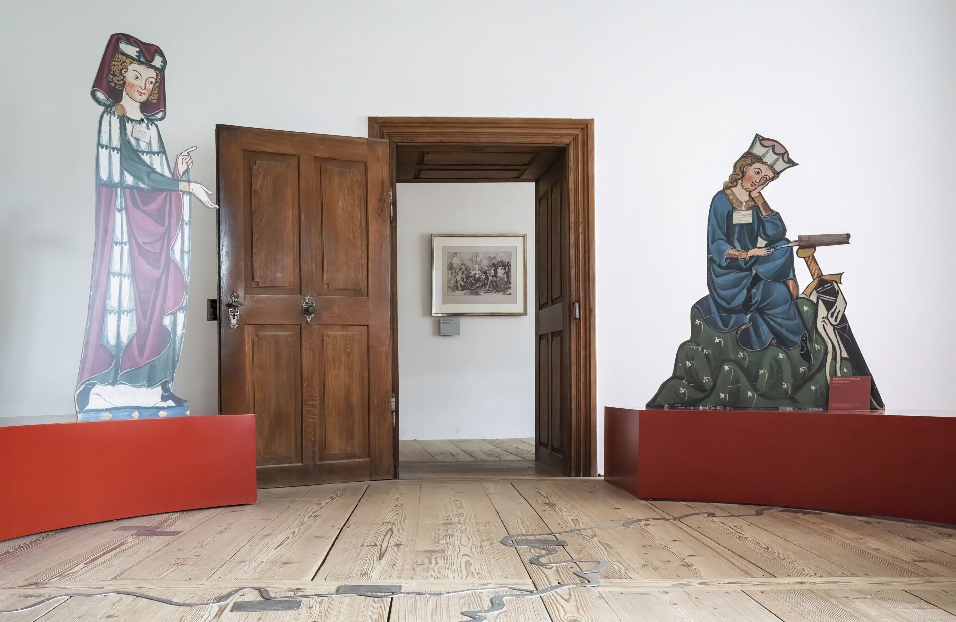 Das Bild zeigt eine Ausstellung von Burg Prunn. Zu sehen ist eine offene Tür, links und rechts neben der Tür sind große Modelle mittelalterlicher Menschen zu sehen.