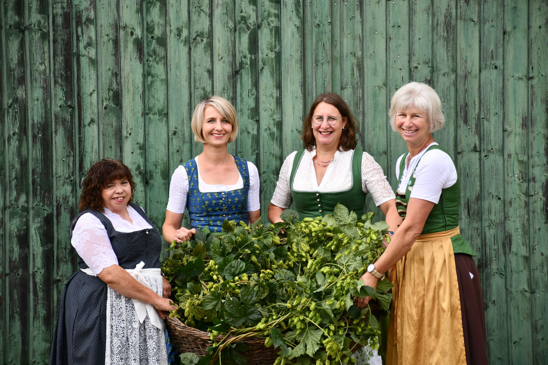 Das Bild zeigt vier Hopfenbotschafterinnen in bayerischer Tracht, welche eine Korb voll frischer Hopfendolden in die Kamera zeigen.