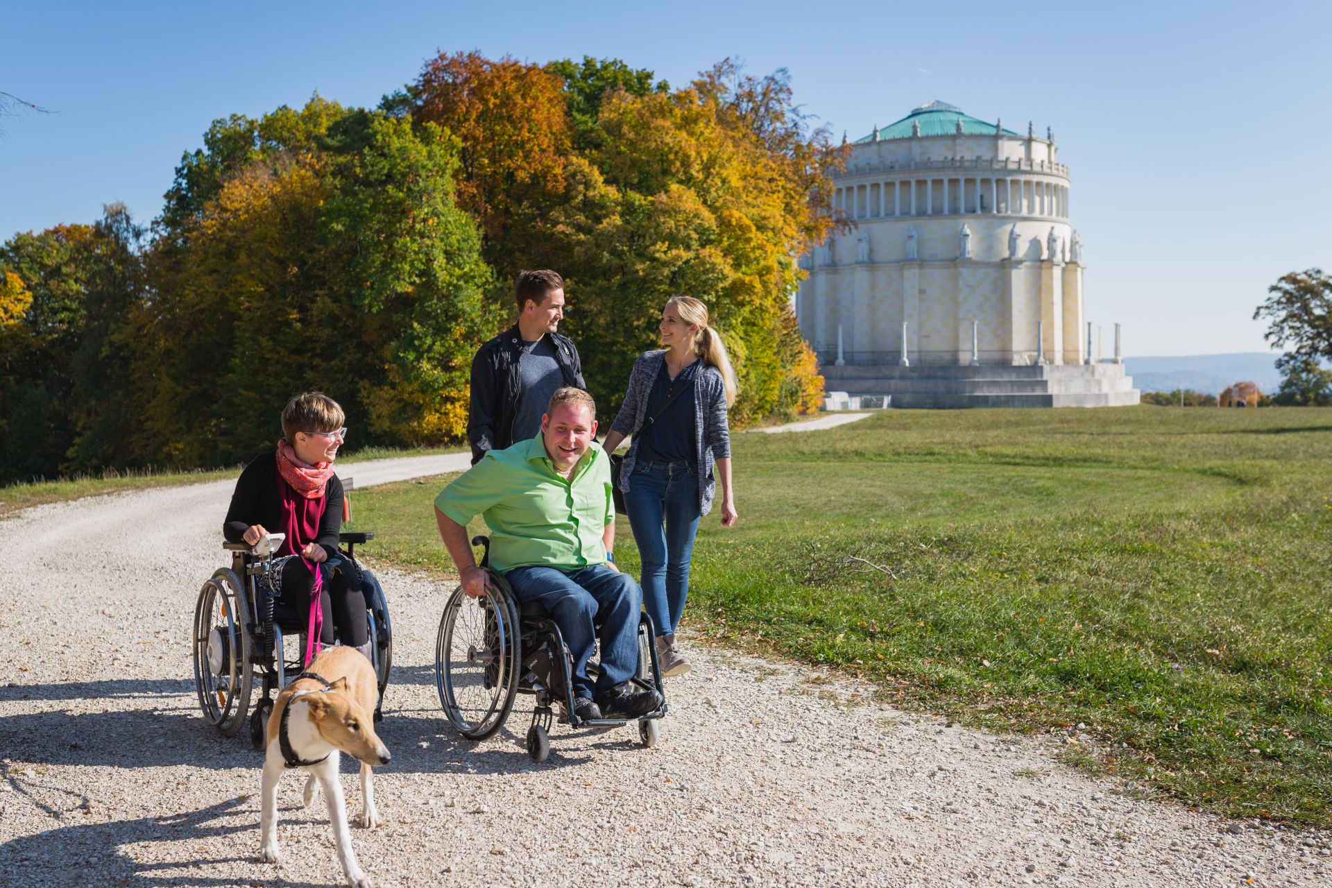 Eine kleine Gruppe mit zwei Rollstuhlfahrern spaziert vorbei an der Befreiungshalle Kelheim.
