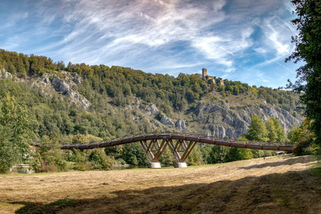 Im Vordergrund befindet sich die Holzbrücke Tatzlwurm und dahinter auf einem Felsmassiv die Burgruine Randeck in Essing.