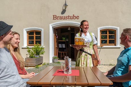 Die Bedienung bringt den Gästen im bayerischen Dirndl gefüllte Biergläser an den Tisch im Biergarten.