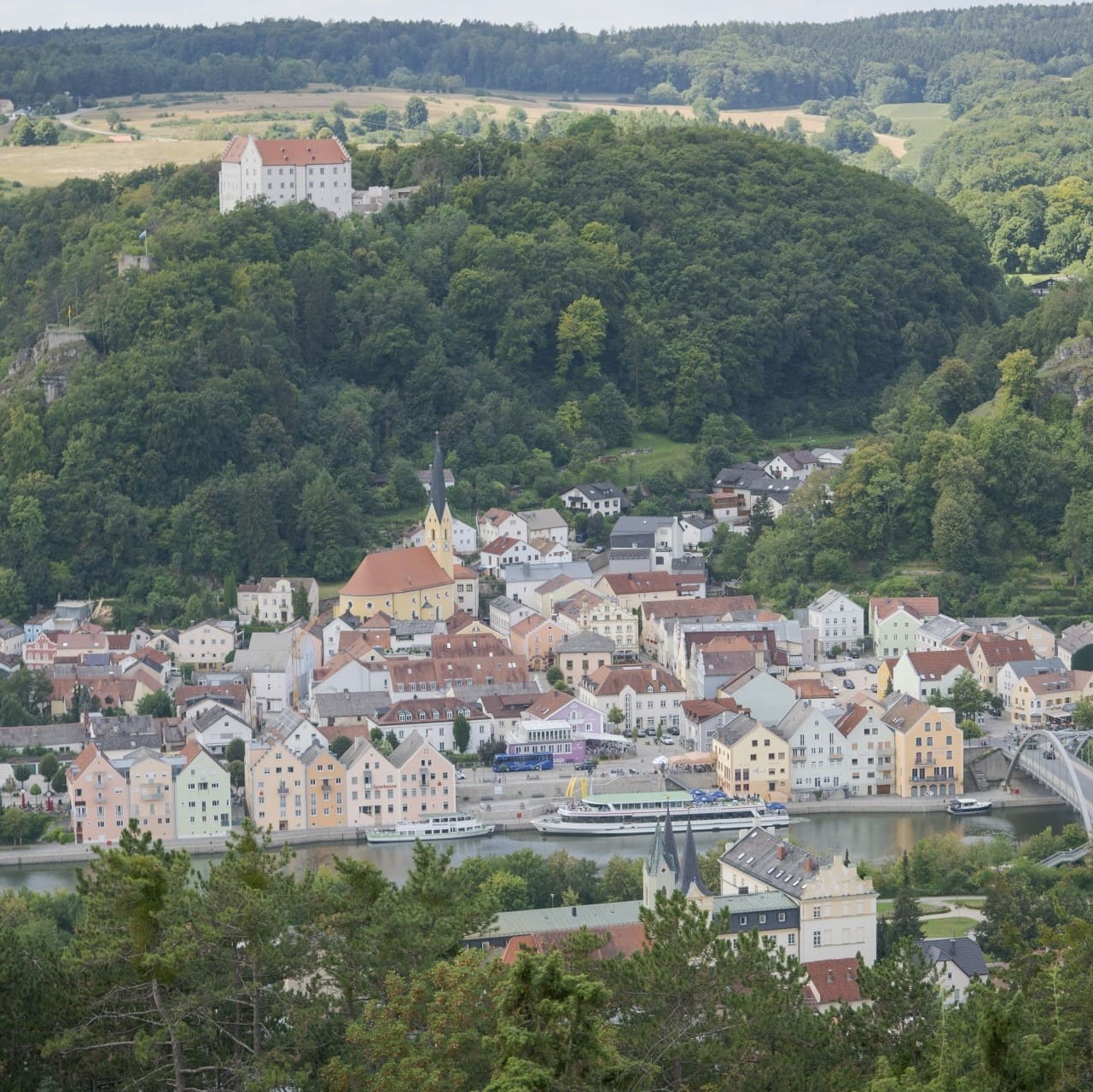 Blick auf die im Tal liegende Stadt Riedenburg. Hoch über der Stadt erhebt sich die Rosenburg. Links von ihr steht die Burgruine Rabenstein und rechts die Burgruine Tachenstein.