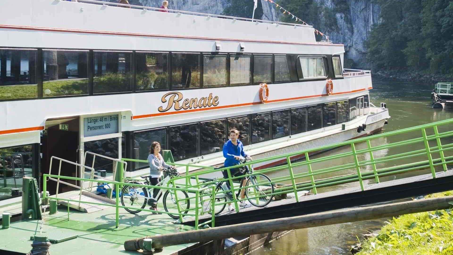 Eine Frau und ein Mann gehen mit ihren Fahrrädern von Bord eines Ausflugsschiffes in Weltenburg.