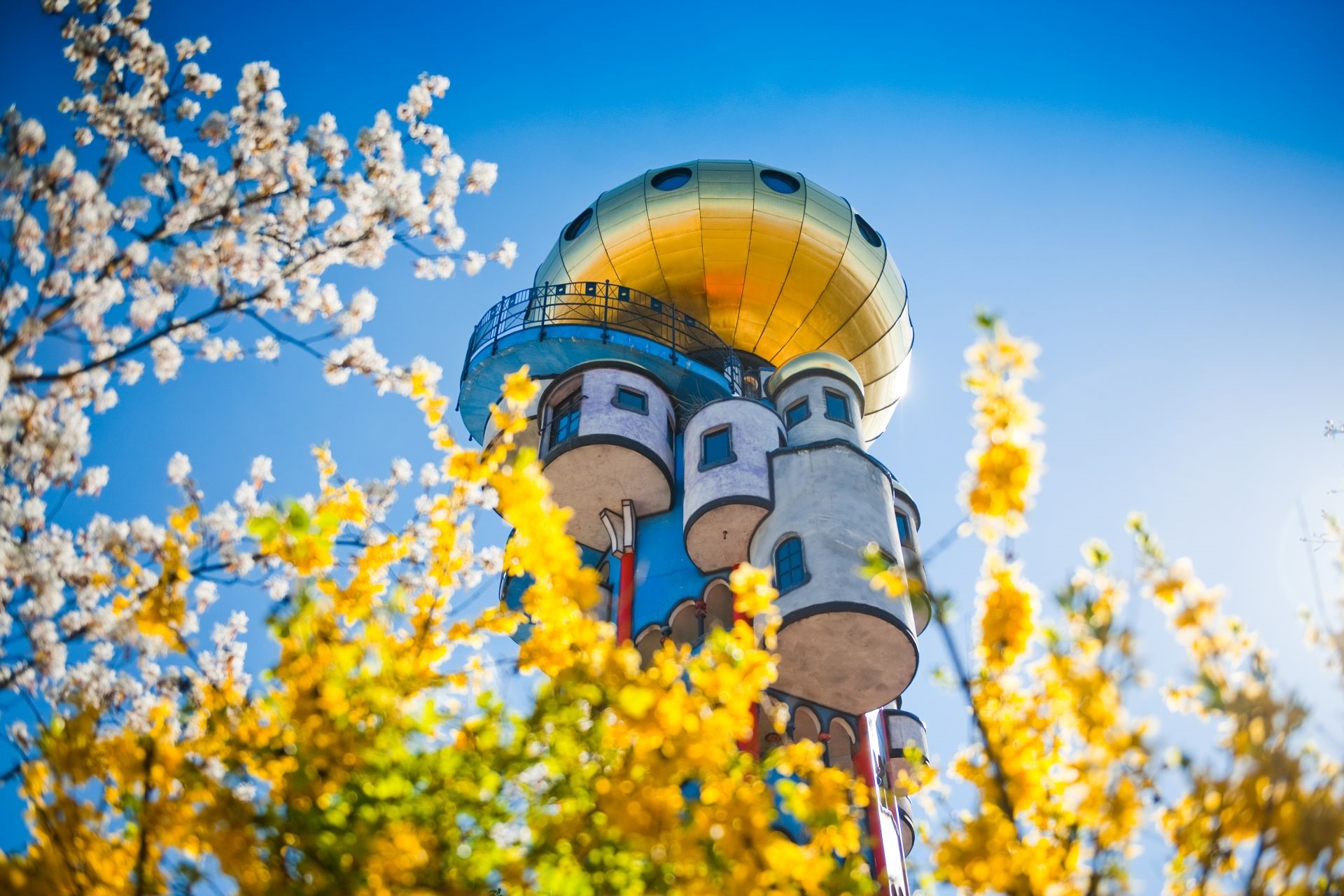 Der Kuchlbauer Turm in Abensberg strahlt mit seiner goldenen Kuppel zwischen bunten Frühlingsblüten hindurch.