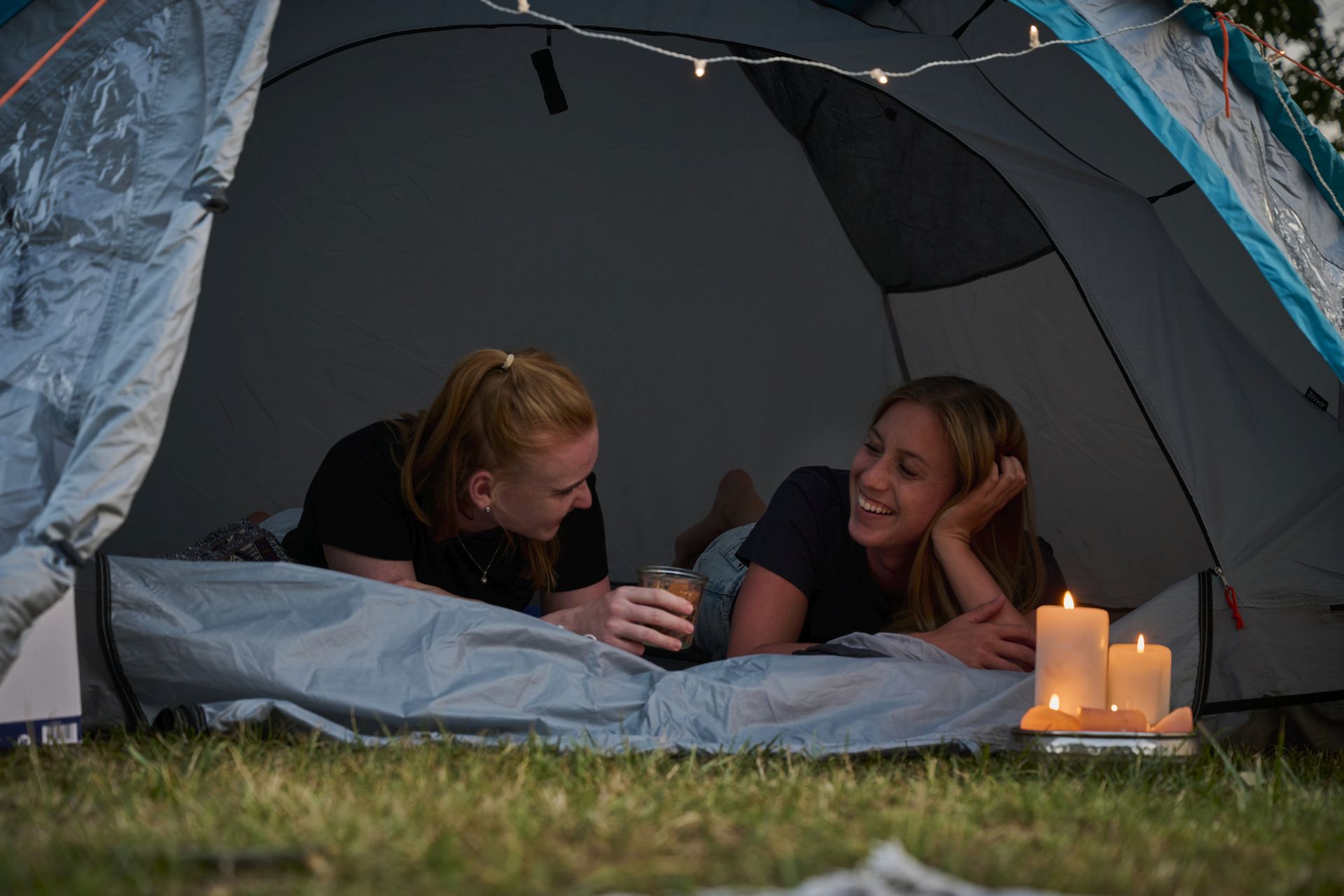 Zwei junge Frauen liegen am Abend in ihrem Zelt und unterhalten sich. 
