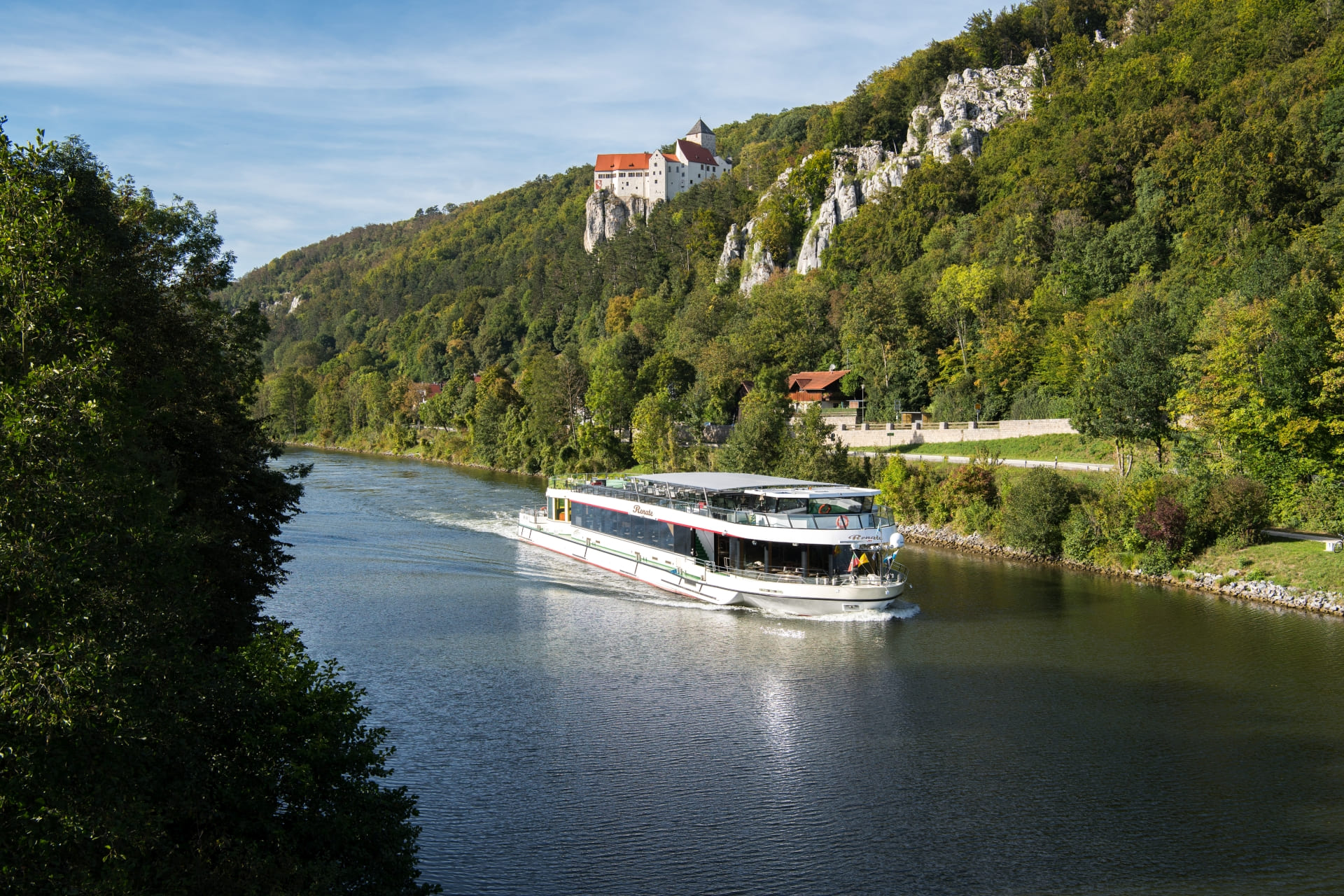Auf dem Main-Donau-Kanal fährt ein Ausflugsschiff von Riedenburg nach Kelheim. Rechts ist die Burg Prunn zu sehen, die auf einem Felsen steht. 
