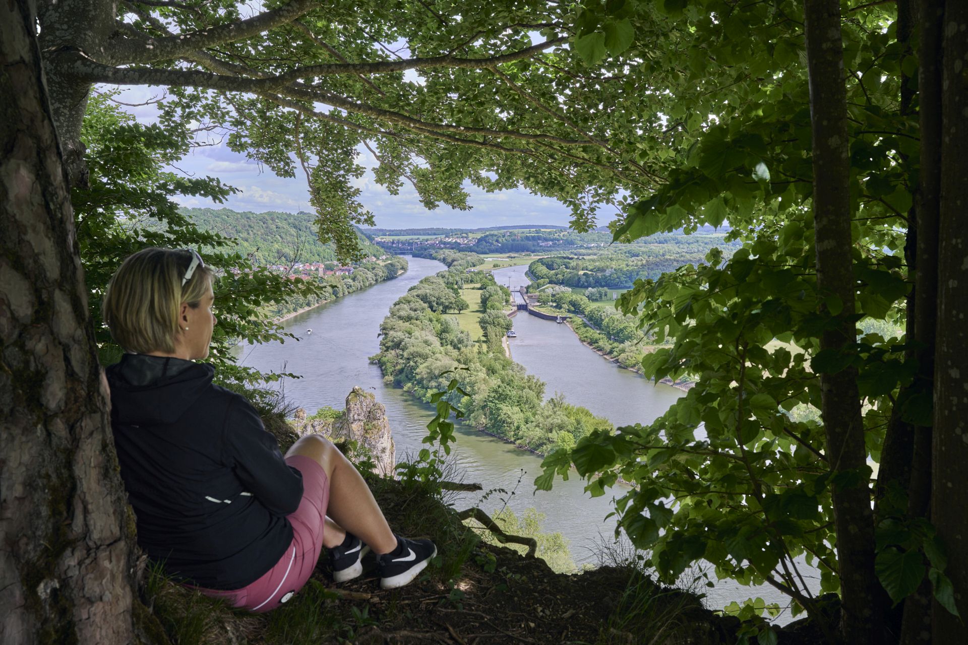 Eine Wanderin sitzt im Sommer unter einem Baum und genießt den Ausblick auf das Donautal bei Oberndorf.