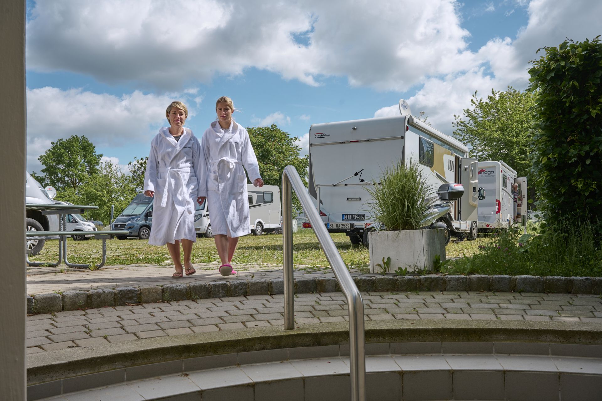 Zwei junge Frauen gehen in weißen Badmänteln vom Wohnmobilstellplatz in die Kaiser-Therme Bad Abbach