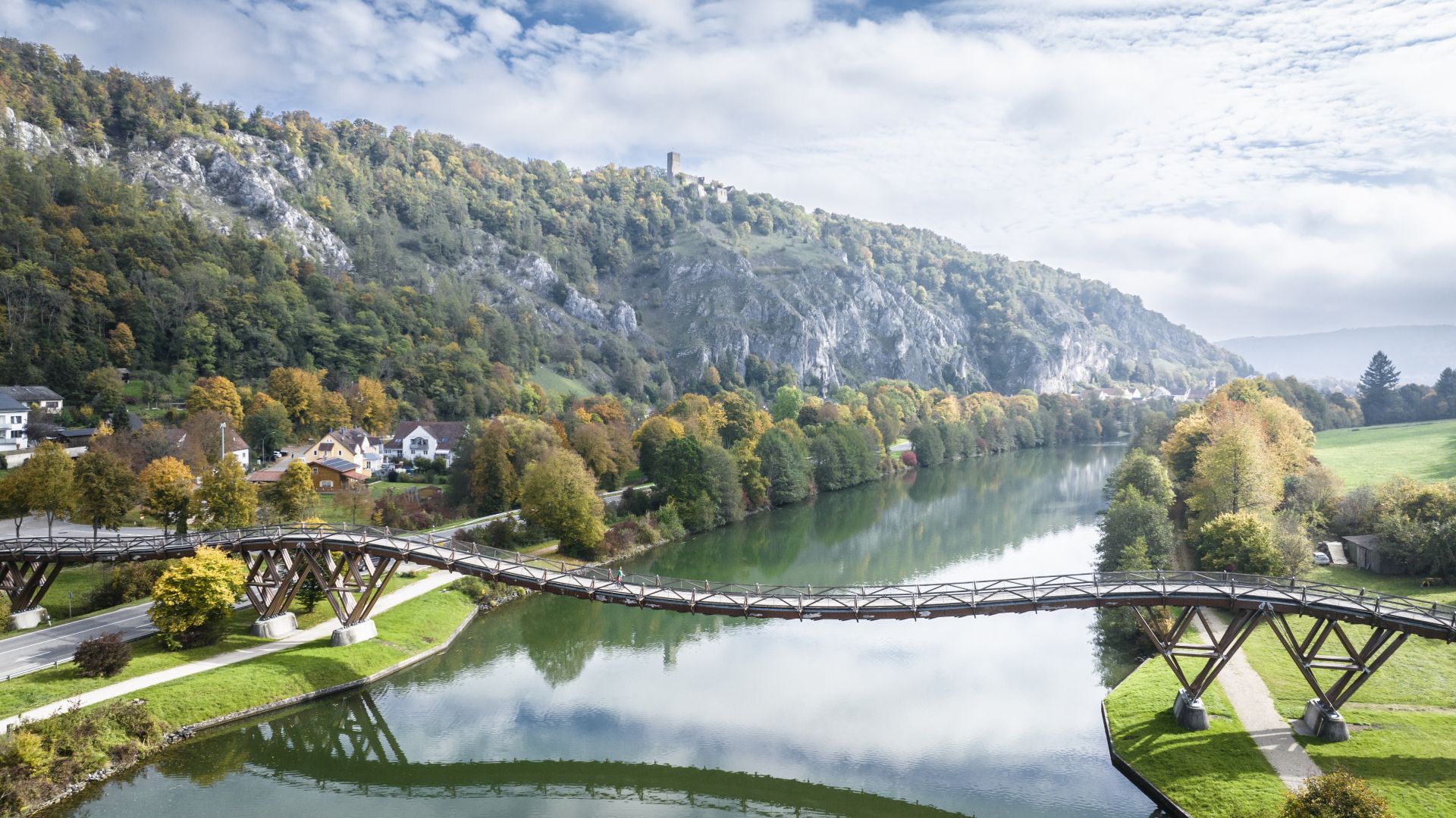 Blick von oben auf die geschwungene Holzbrücke Tatzlwurm, den Main-Donau-Kanal und die grünen Hänge des Altmühltals.