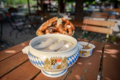 Zu sehen ist ein bayerischer Porzellantopf mit Weißwürsten im heißen Wasser. 